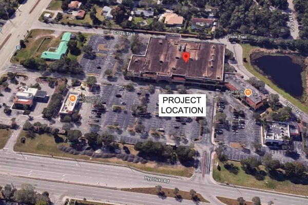 Aerial view of a commercial plaza with parking lots, nearby roads, and a marked project location.